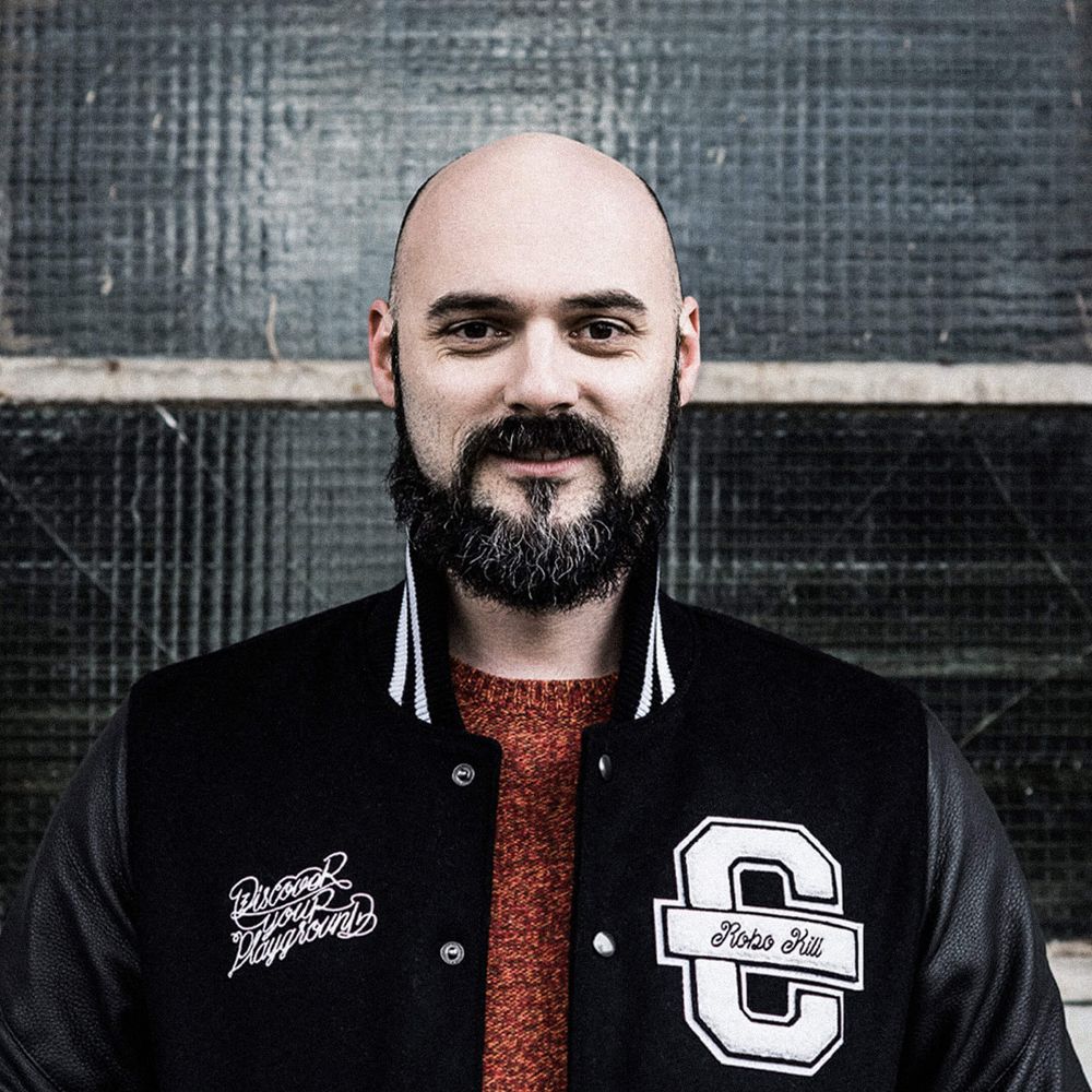 Auf dem Bild ist Alex zu sehen. Er trägt eine schwarze Cromatics-Jacke und lächelt leicht.