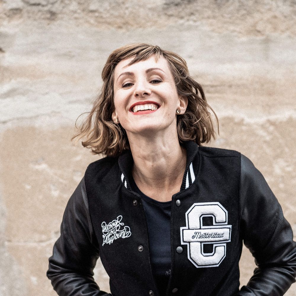 Hier ist Anne zu sehen. Sie trägt eine schwarze Cromatics-Jacke und lacht herzlich in die Kamera.