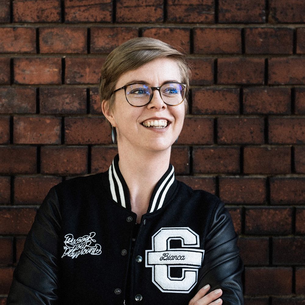 Hier ist Bianca zu sehen. Sie trägt eine schwarze Cromatics-Jacke und lächelt mit dem Blick nach oben rechts.