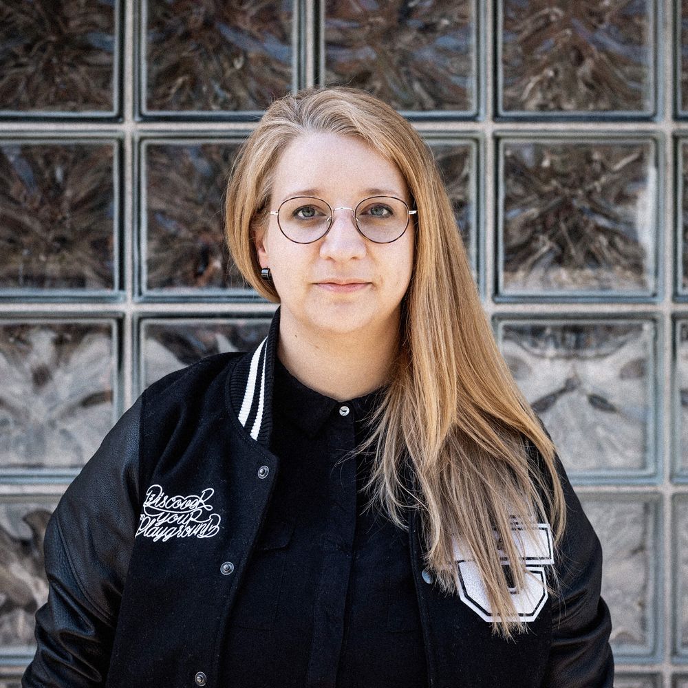 Auf dem Bild ist Katha zu sehen. Sie trägt eine schwarze Cromatics-Jacke und lächelt leicht.