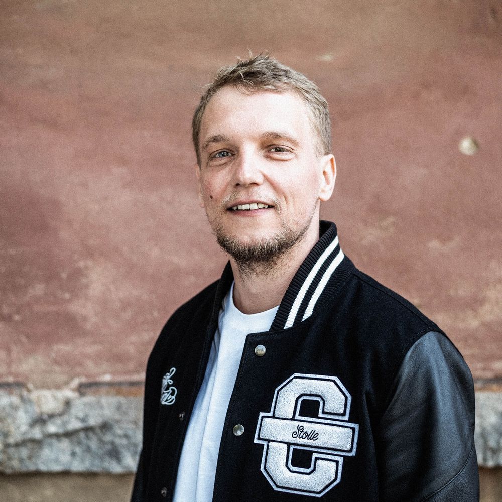 Auf dem Bild ist Stolle zu sehen. Er trägt eine schwarze Cromatics-Jacke und lächelt leicht.