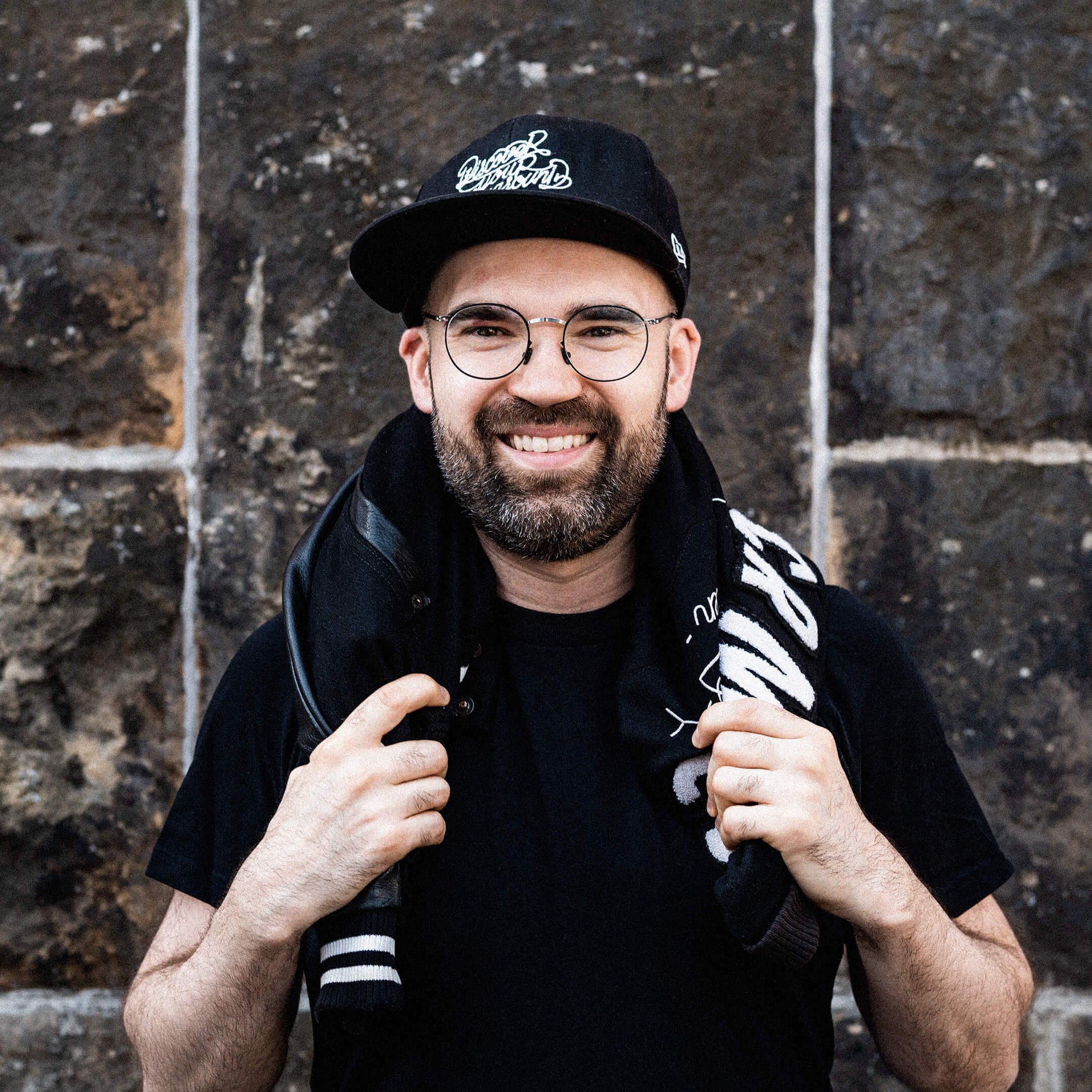 Hier ist Andreas zu sehen. Er hat seine Cromatics-Jacke über seinen Nacken gelegt und lächelt.