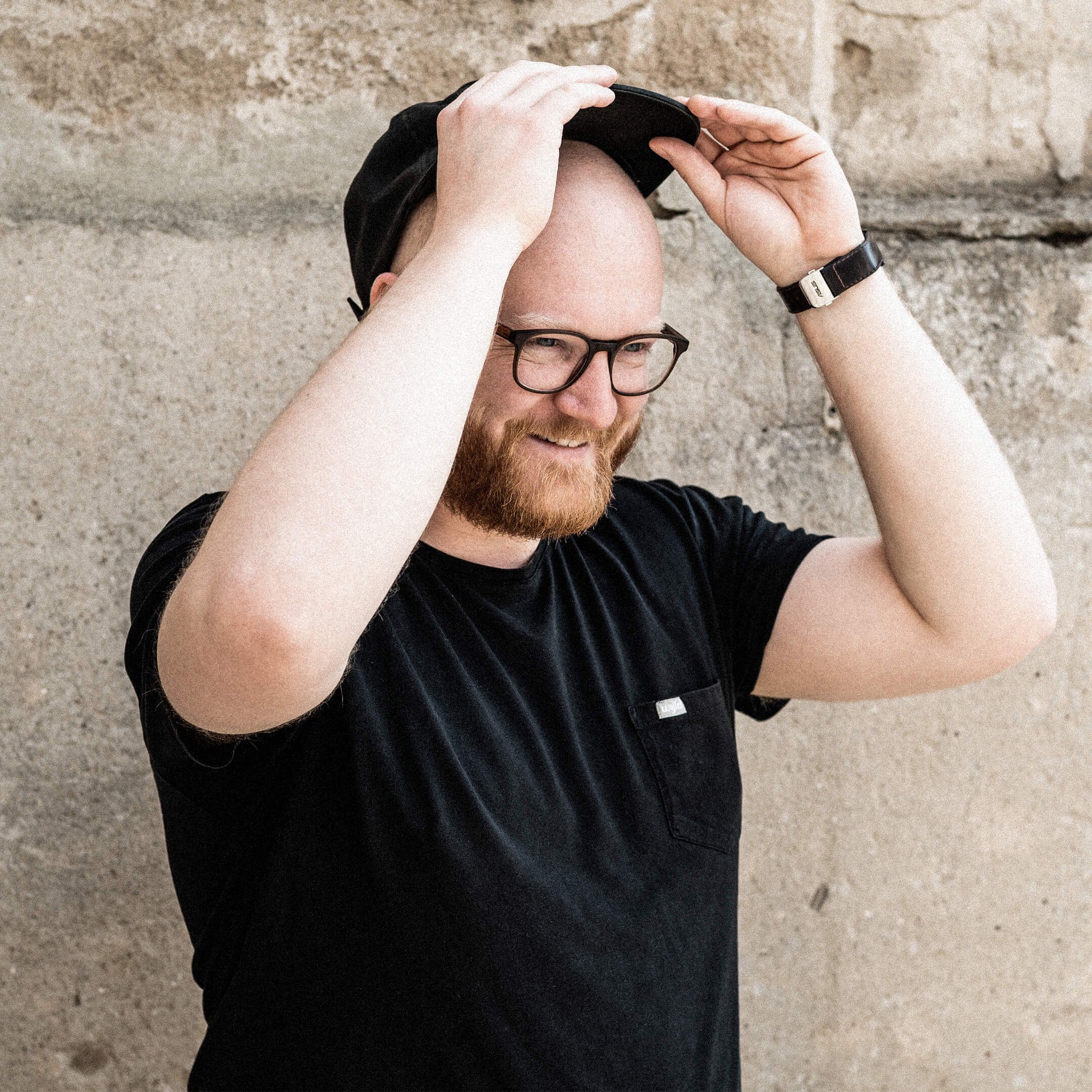 Auf dem Bild ist Jonny zu sehen. Er setzt sich gerade sein Cap auf und schaut fröhlich nach rechts.