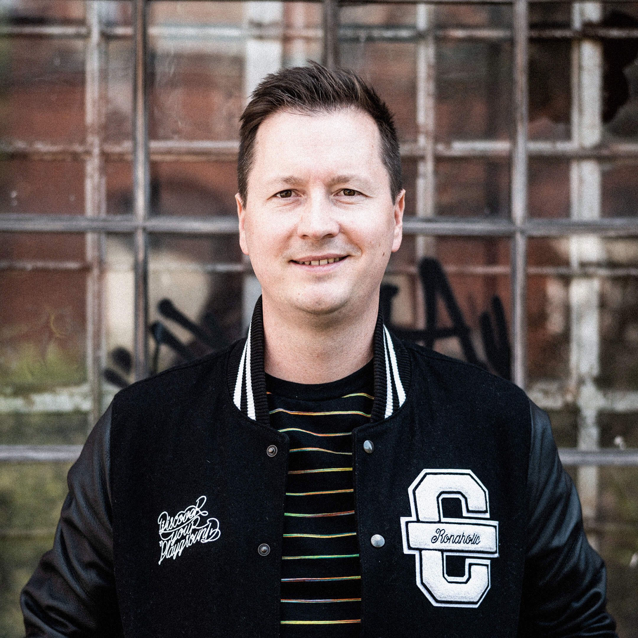 # Auf dem Bild ist Ron zu sehen. Er trägt eine schwarze Cromatics-Jacke und lächelt verschmitzt.