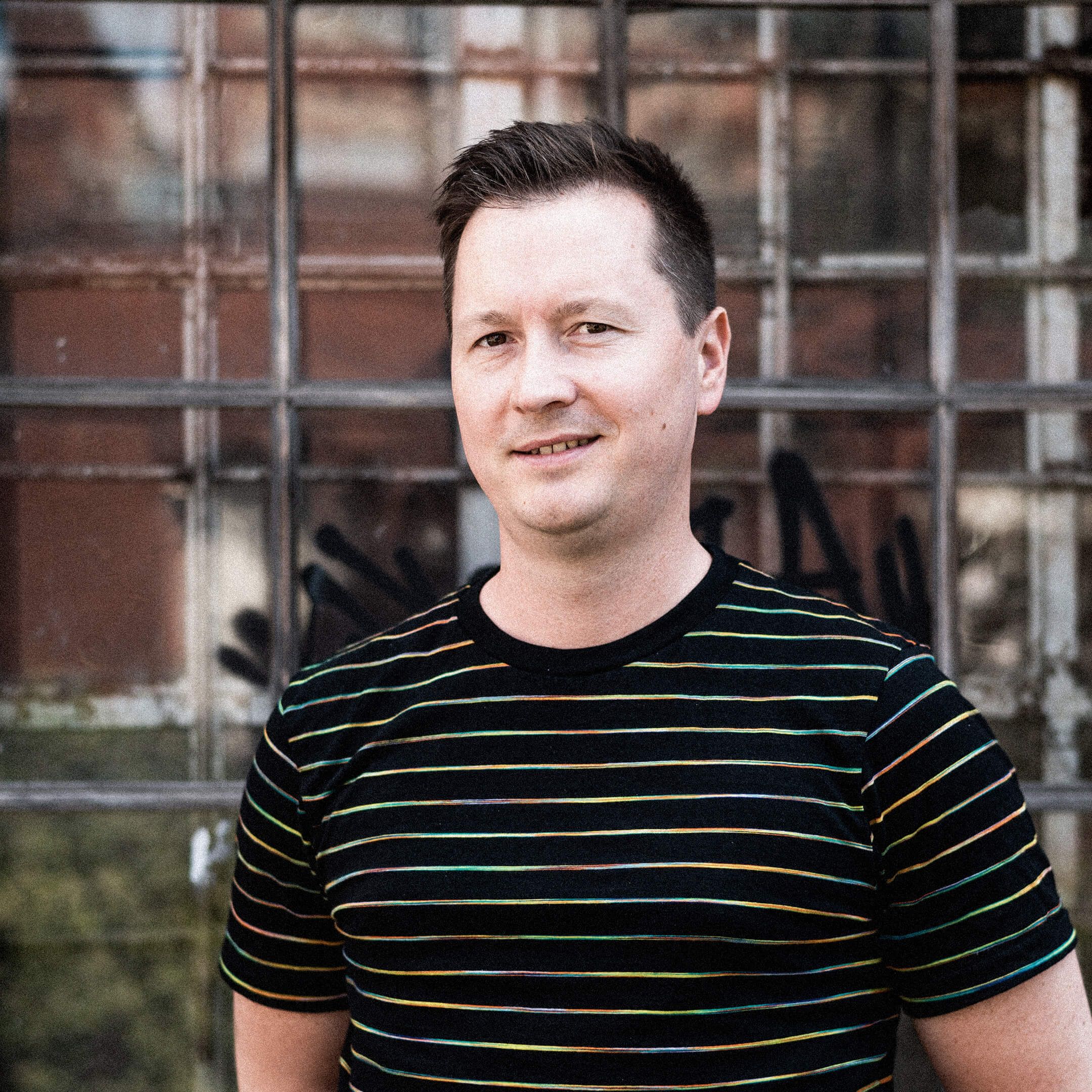 Auf dem Bild ist Ron zu sehen. Er trägt ein schwarzes Shirt und lächelt leicht.