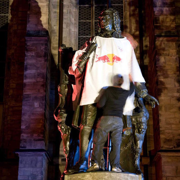 Person stülpt nachts der leipziger Statue von Johann Sebastian Bach das RB-Trikot über